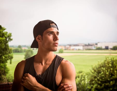 A man in a black shirt and a black hat. Photo of a stylish young man in a black shirt and hat in front of a distant grass field