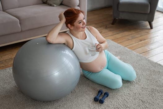 Pregnant woman drinks water after workout on fitness ball