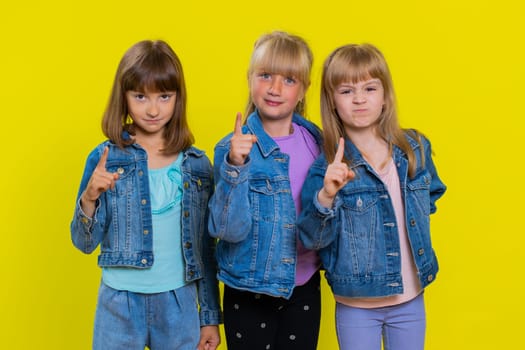 Quarrel. Displeased teenage girls gesturing hands with irritation and displeasure, blaming scolding for failure, asking why this happened. Children sisters. Three siblings kids on yellow background