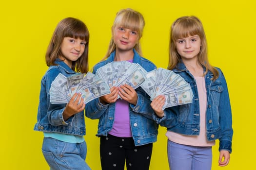 Rich happy teenage girls waving money dollar cash banknotes bills like a fan, success business career, lottery game winner, big income, wealth, donation. Little children sisters. Three siblings kids