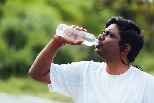 Close up Asian young sport runner black man wear athlete headphones he drinking water from a bottle after running at the outdoor street health park, healthy exercise workout concept