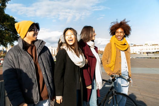 Multiracial friends walking around city, enjoying winter afternoon together laughing and talking. College student friendship concept.