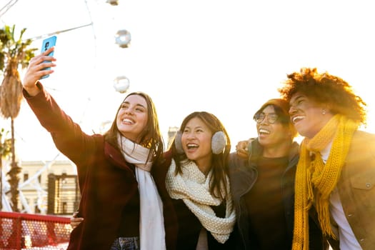 Happy multiracial group of smiling and cheerful college friends taking selfie together in a sunny winter day in the city using mobile phone. Technology and lifestyle concept.