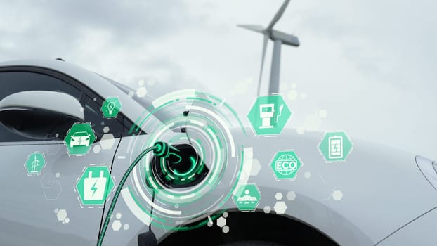 Electric car recharging energy from EV charging station display futuristic smart battery status hologram by EV charger plug cable in wind turbine farm. Alternative clean energy sustainability. Peruse