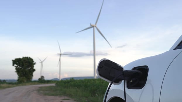 Progressive future energy infrastructure concept of electric vehicle being charged at charging station powered by green and renewable energy from a wind turbine in order to preserve the environment.