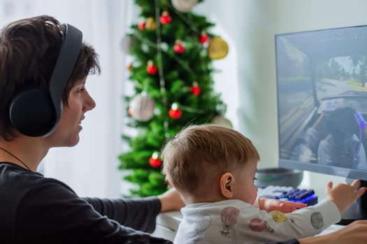 A teenager in headphones holding a baby sitting in front of a computer, the child laughs. High quality photo