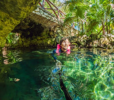 09.12.24, Playa Del Carmen, Mexico: Man tourist standing in the water of a cenote at Xcaret park wearing a marked life jacket. Mexican tourism in natural parks. Adventure, relaxation, and eco-tourism concept in Quintana Roo.