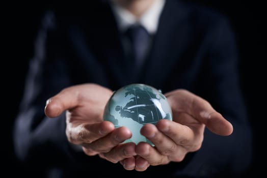 Businessman in suit holding glass globe with world map closeup. International financial relations concept