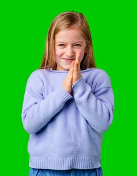 A young child in a cozy sweater and blue cargo pants poses with hands clasped in studio