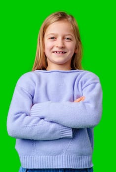 Child wearing a blue sweater and light blue pants stands confidently in front of a green background in a studio