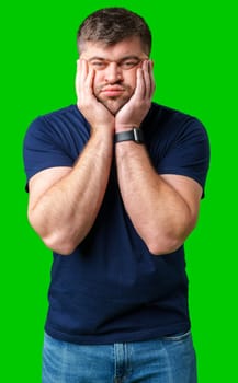 Young man with a contemplative expression leaning against green backdrop while resting his head on his hand in studio