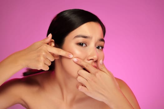 A model demonstrates effective acne treatment techniques by using her fingers to target blemishes on her face, all set against a vibrant pink background.