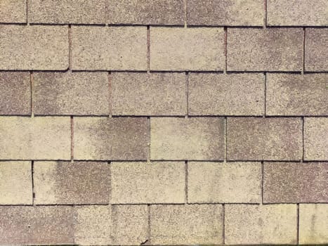 A close-up view of roofing shingles displays a textured surface with a neutral color palette under bright daylight.
