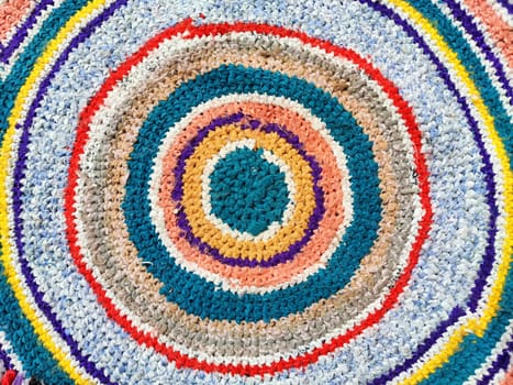 A vibrant circular rug features concentric patterns in a variety of colors, adding warmth and style to an indoor space, perfect for cozy settings.