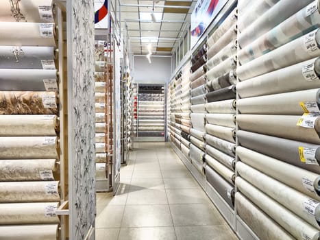 Kirov, Russia - August 08, 2023 - Brightly lit store aisle showcasing a diverse range of wallpapers neatly rolled and displayed for customer selection.