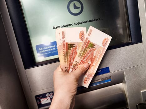 Kirov, Russia - October 08, 2024: A person at an urban ATM is withdrawing cash, displaying several banknotes while waiting for the transaction.