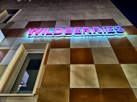 Kirov, Russia - November 12, 2024: Illuminated sign of the Wildberries marketplace shines on the building exterior during nighttime in a vibrant urban environment.