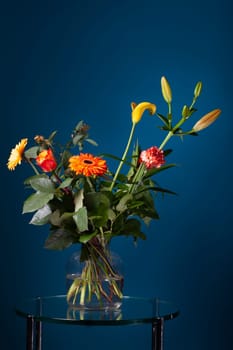 Fresh bouquet of flowers in a glass vase on a glass table with a dark blue background