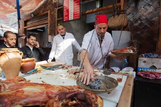 Marrakech, Morocco – February 25, 2023: Butcher weighs roast meat in the medina or souk of Marrakech