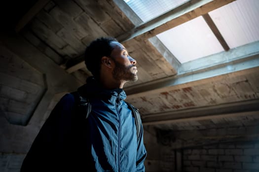 A contemplative man thoughtfully gazes upwards towards a skylight window situated within a dimly lit, quiet space