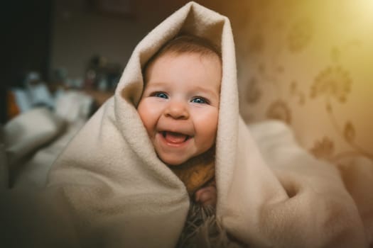 Smiling baby girl crawling on bed under the blanket. Adorable kid portrait. 5 month old child. Childhood concept. High quality photo