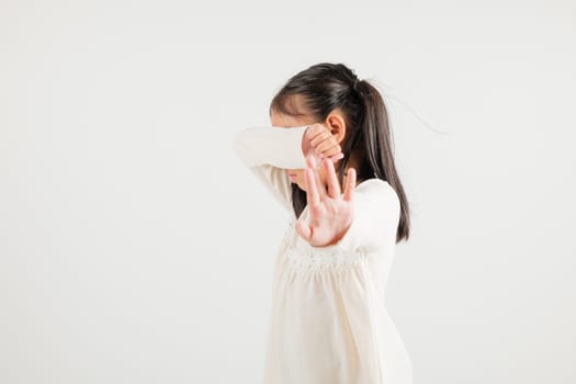 Asian portrait cute young kid girl smiling doing show stop sign gesture with palm of hand but unhappy face studio shot isolated on white background, kindergarten children doubt with copy space