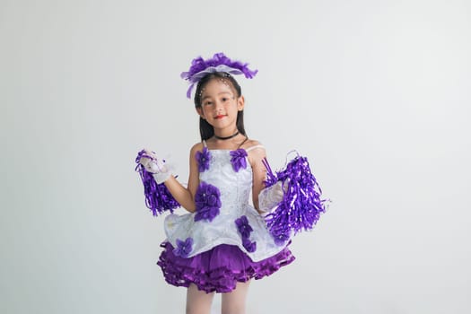 Cheerful young cheerleader girl in a purple and white outfit, holding pom-poms. Energetic studio shot on a white background, full of joy and excitement. cheerleader kid