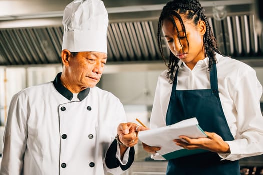 In a restaurant kitchen an Asian senior chef educates multiracial students emphasizing teamwork learning and note-taking. Professional training in action. Food Edocation