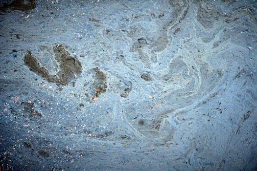 Foam and debris floating on polluted water create abstract shapes, highlighting environmental damage