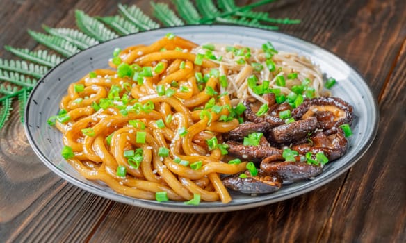 A portion of udon noodles with soy unagi mirin ginger sauce, shiitake and enoki mushrooms, and green onion