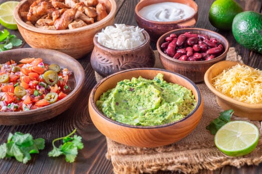 Bowls with burrito components: salsa, cheese, chicken, sour cream, lime, cilantro, rice, guacamole, beans, avocado, and chips