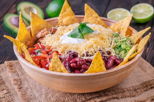 A large burrito bowl filled with chicken, rice, beans, guacamole, salsa, cheese, sour cream, and tortilla chips