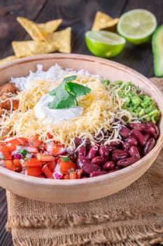 A large burrito bowl filled with chicken, rice, beans, guacamole, salsa, cheese, sour cream, and tortilla chips