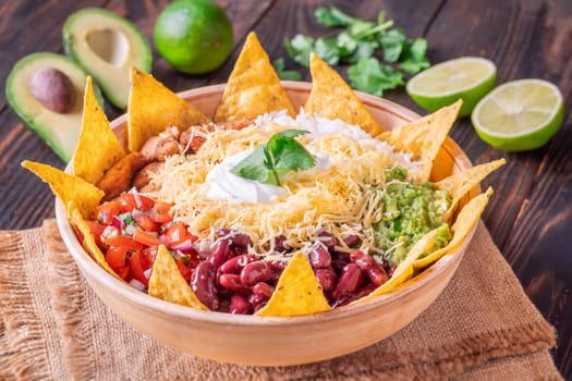 A large burrito bowl filled with chicken, rice, beans, guacamole, salsa, cheese, sour cream, and tortilla chips
