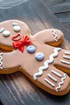 A large gingerbread man cookie with a red bow on a wooden cutting board