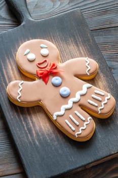 A large gingerbread man cookie with a red bow on a wooden cutting board