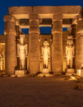 Massive numerous stone columns supporting roof with statues in Luxor Temple in Egypt illuminated at night