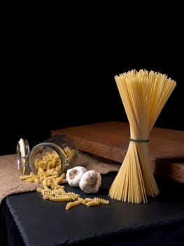 A still life photo of dried spaghetti and spiral noodles with two bulbs of garlic.