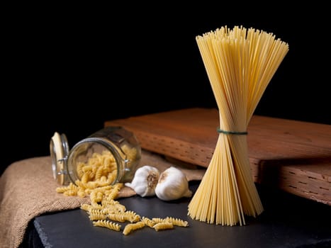 A still life photo of dried spaghetti and spiral noodles with two bulbs of garlic.