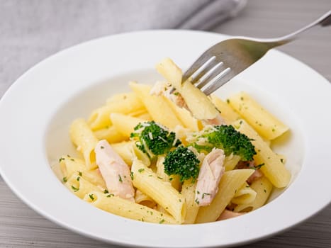 Getting a fork full of delicious penne oil pasta covered with parmesan cheese, broccoli, and bits of chicken.