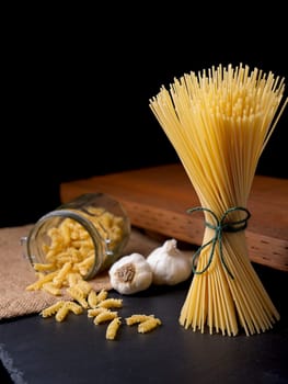 A still life photo of dried spaghetti and spiral noodles with two bulbs of garlic.