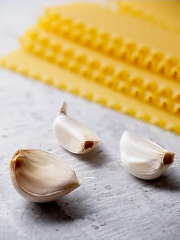 A closeup studio photo of three cloves of garlic and dried lasagna noodle strips.