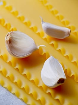 A closeup studio photo of three cloves of garlic and dried lasagna noodle strips.