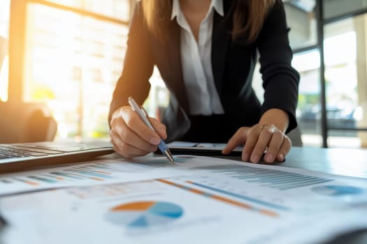 A business professional is focused on analyzing financial reports and charts in a modern office setting with a laptop.