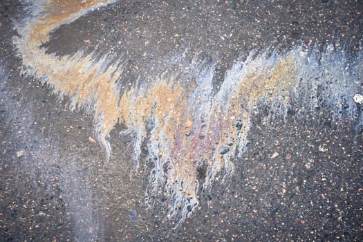 Moist pavement in a parking lot, highlighting a motor oil leak from a vehicle.
