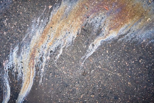 Gasoline or oil spill creating colorful patterns on asphalt road.