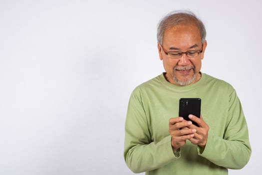 Portrait smiling Asian older man smiling holding a cell phone studio shot isolated on white background. elderly typing message on mobile phone in hand. Concept of connection and communication