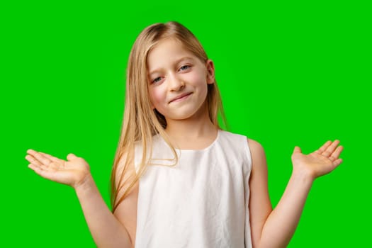 A young girl with long hair smiles and shrugs while standing against a bright green background in studio