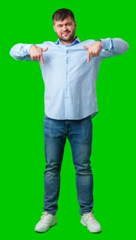 Man in a blue striped shirt and jeans gesturing downward against a bright green background in studio