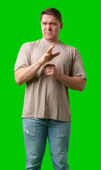 Young man making a disgusted expression while standing against a bright green background in studio